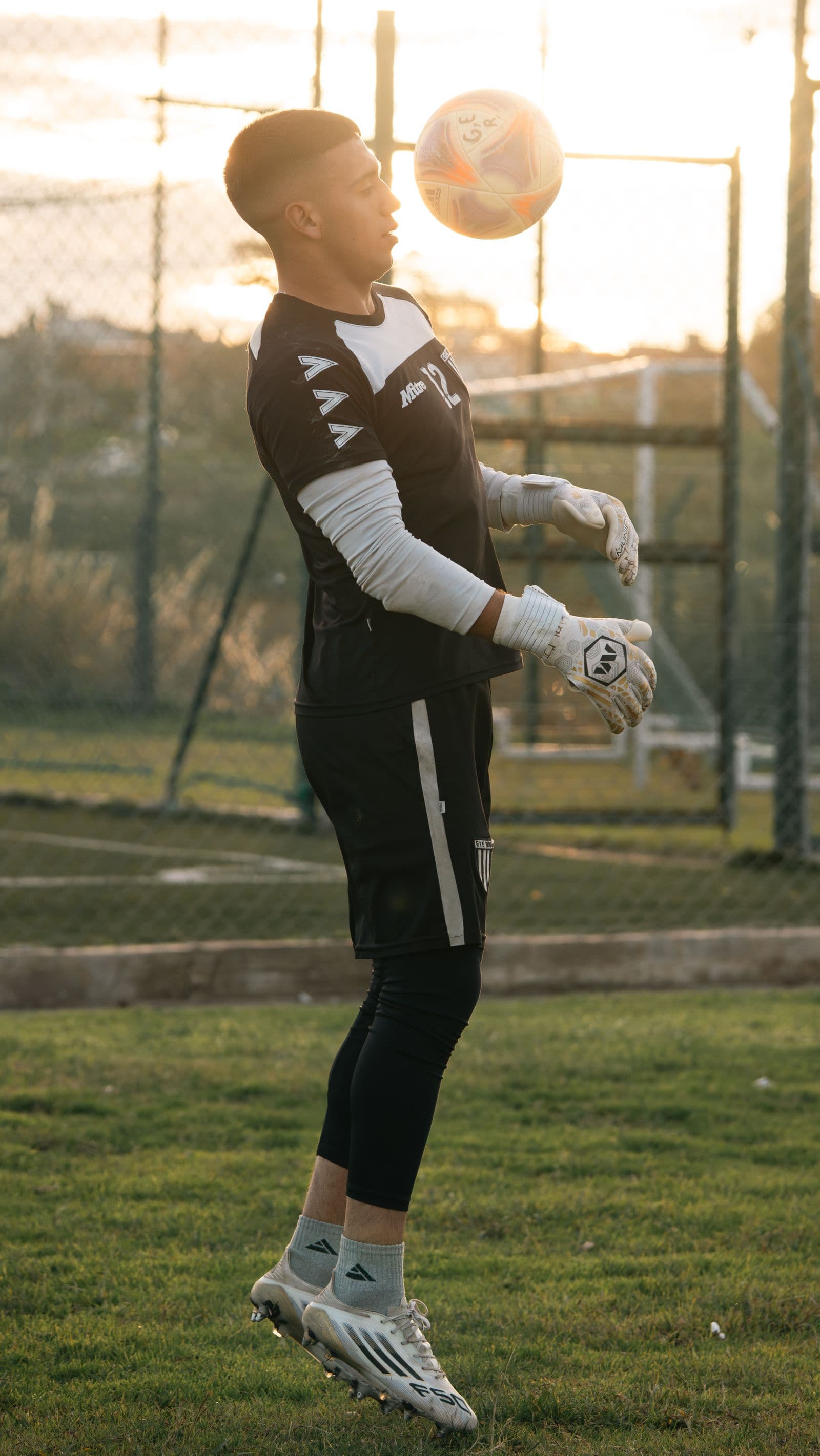 A goalkeeper in black working the ball at golden hour